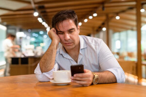 Man at a coffee shop engrossed in mobile phone, reminiscent of modern customer service trends.