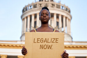 A woman in front of the Capitol building holds up a sign demanding cannabis legalization.