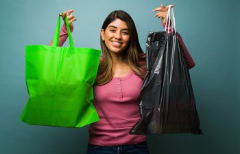Recycling is good for the environment. Beautiful woman smiling while holding a reusable green bag and a plastic garbage bag to recycle